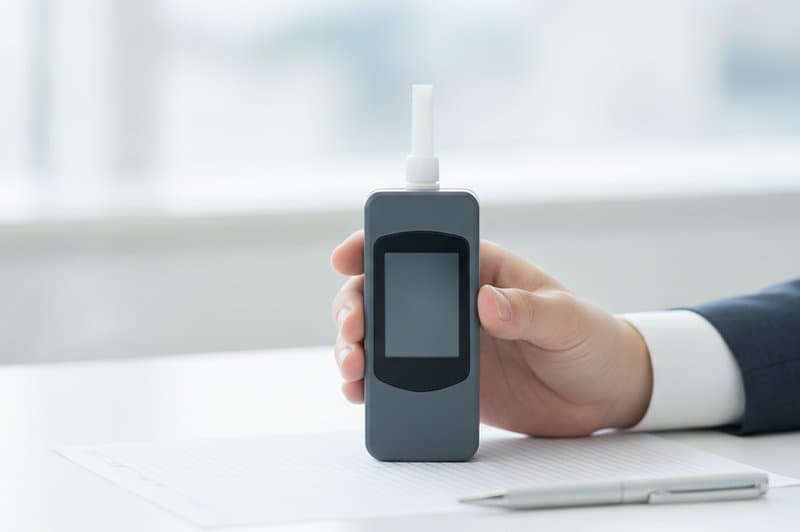 アルコール検知器とスマートフォンを持つ手元