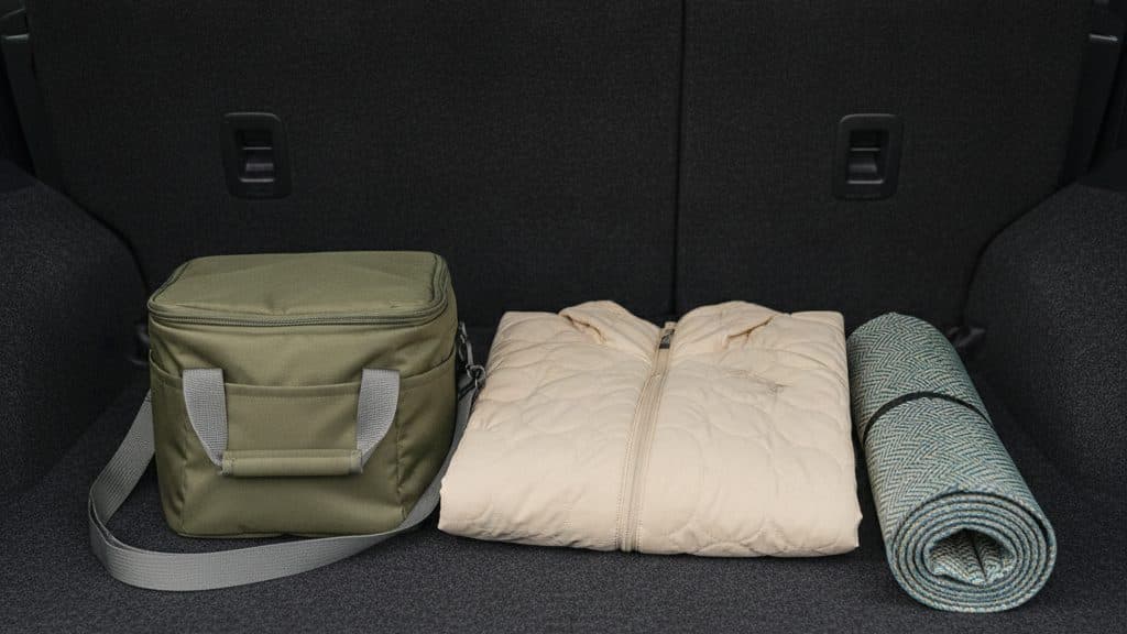 車の荷室の床に、オリーブ色の保冷バッグ、たたんだクリーム色のキルティングの上着、丸めたレジャーシートが並んでいる